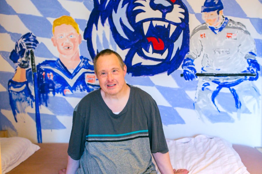 Ein Mann sitzt aufm Bett, 2 Hockeyspieler als Wandhintergrund